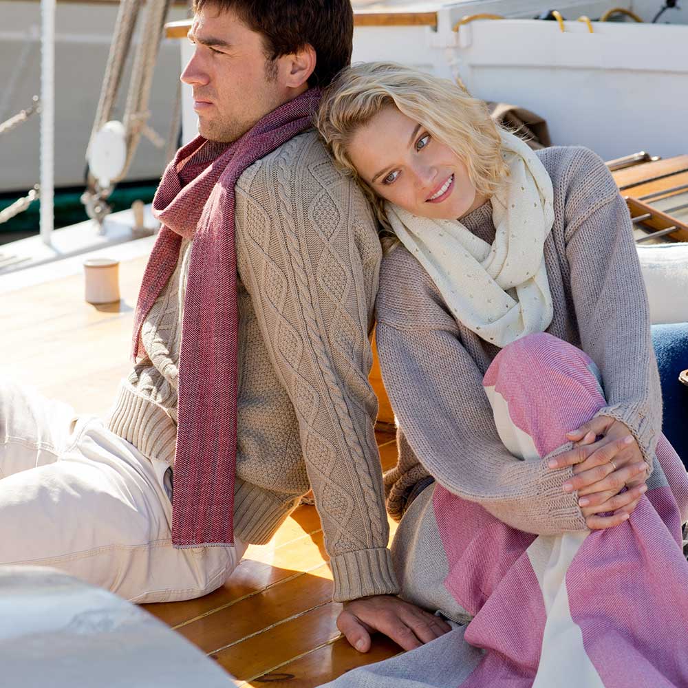 Swans Island Handwoven Camden Scarves. Made in Maine with hand-dyed merino wool. These beautiful scarves are made with organic merino wool which is dyed with all-natural dyes. Shown here on male model in Mulled cider. Female model wears our Coastal Cowl in ivory with our Maine Coast Throw in Raspberry.