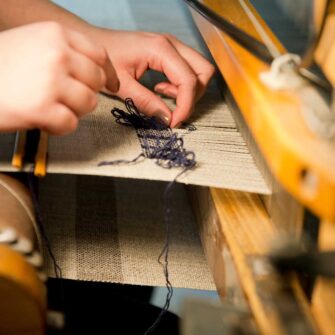 Closeup of weaver's hands adding the Swans Island weaver's mark on an Island Throw.