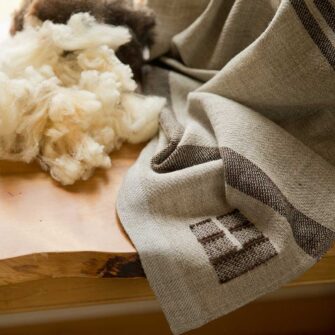 Swans Island Company's Island Throw captures the essence of the Maine. Woven by hand in our Maine studio with locally sourced island wool. Shown here, our signature weaver's mark on a grey with brown throw. This fleece is from the local farm and was spun into yarn for this blanket.