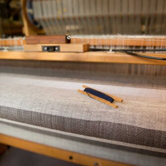 Swans Island Company's Island Throw captures the essence of the Maine. Woven by hand in our Maine studio with locally sourced island wool. Shown here on the loom in grey with brown stripe.