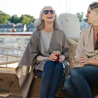 Women wearing capes and laughing while enjoying drinks outside by the harbor