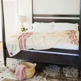 Swans Island Grace Blanket. Handwoven in Maine. 100% wool. Shown here in natural with red tripes on a king bed.