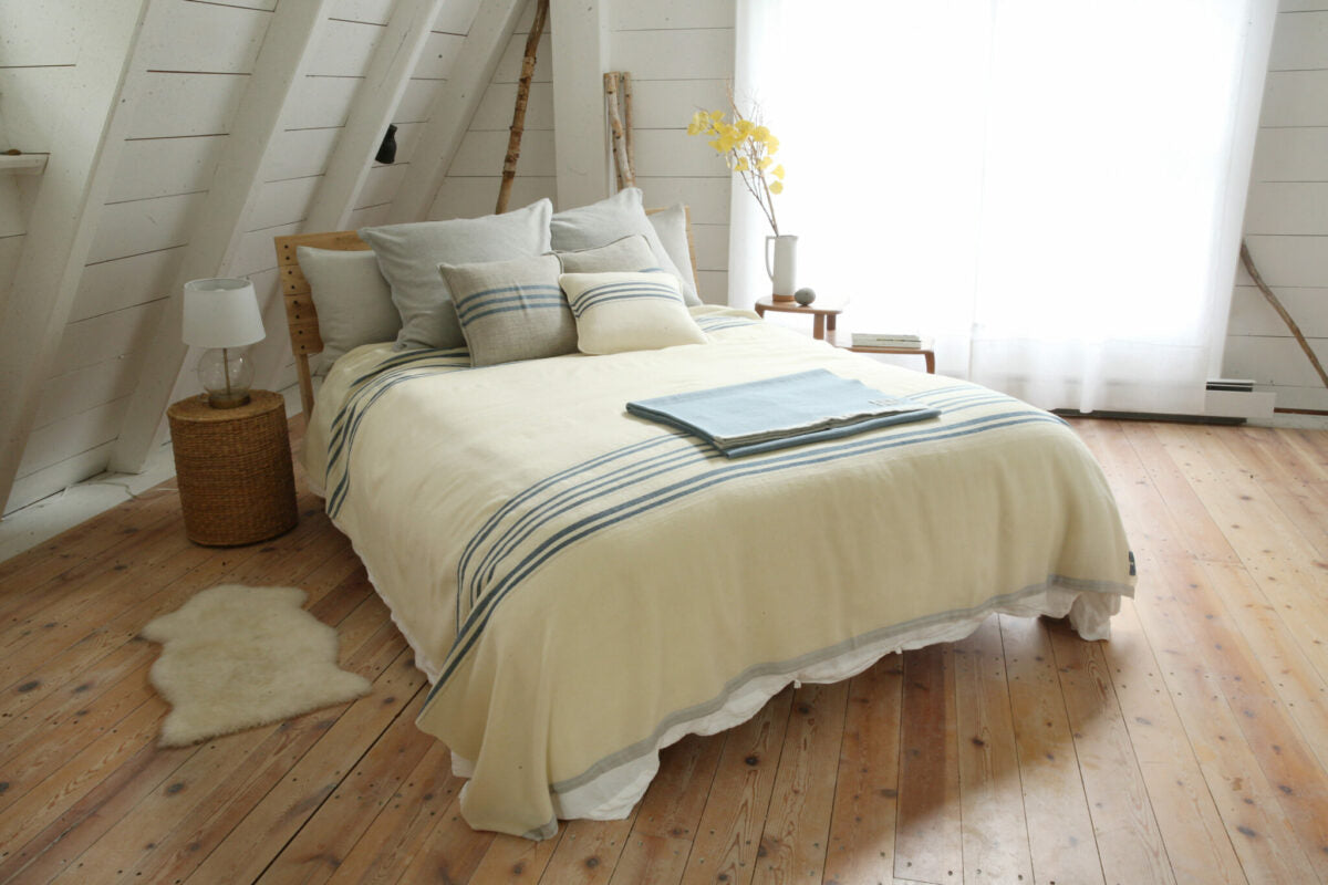 The best-selling natural with indigo stripes Grace blanket is paired with coordinating pillows for a classic yet modern bedroom setting in this classic coastal Maine cottage. All handwoven by Swans Island Company in Maine.
