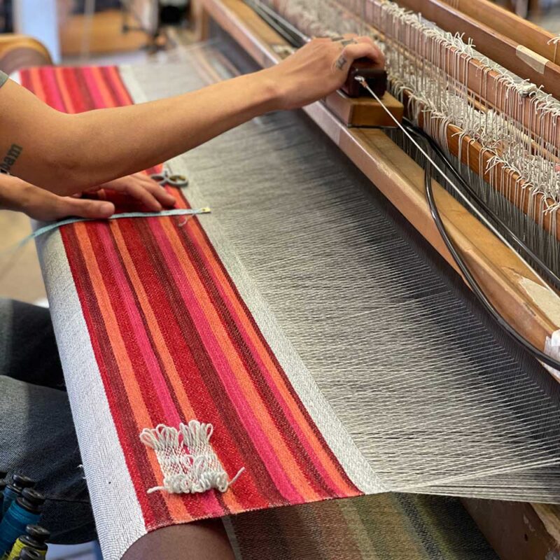 Swans Island Company's Limited Edition Prism Series. Nine rainbow-inspired throws designed by our team of talented weavers. Each throw in this limited edition drop is unique! The "R" in ROYGBIV is the first color to emerge as a rainbow of wool evolves into a new Prism throw on the loom.