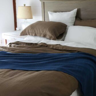 Swans Island Company's Relaxed Linen bedding is made with 100% French linen, stitched in the USA. Shown here, Relaxed Linen duvet set in Mocha paired with Classic Linen Sheet Set in White. Also shown, handwoven Katahdin blanket in Indigo.