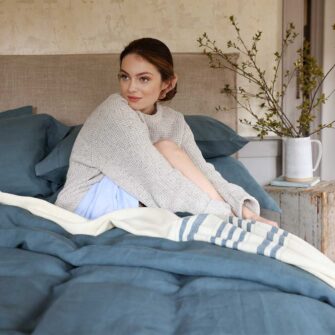 Swans Island Company's Relaxed Linen Bedding Bundle. 100% French linen made in the USA, breathable, soft and regulates temperature as you sleep. Shown here in Aegean with our handwoven wool Grace Blanket in Natural with teal stripes.