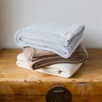 Swans-Island Company's Cashmere Mini-Cable Blankets are woven in Maine with a soft blend of 70% American cotton + 30% Cashmere Shown here in Frost, Hazlenut and Muslin.
