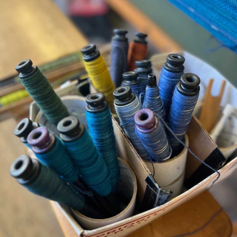 The Swans Island & Eric Hopkins Ltd. Edition Throw 2024. Seventeen beautiful colors of hand-dyed wool are wound onto spindles, waiting to be woven at the Swans Island studio in Northport, Maine.