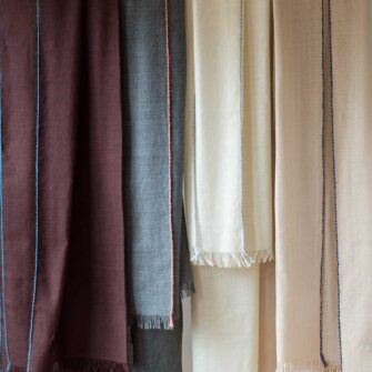 Swans Island Company's Royal Alpaca Whisper Shawl. Made of the softest alpaca with a hint of color woven in at the edges for an unexpected surprise! Shown here in Mahogany, Charcoal, Ivory, and Bisque.