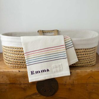 Swans Island Company's Rainbow Borders Baby Blanket. Handwoven in Maine with soft 100% organic merino wool. Comes in a signature linen box, perfect for gifting. Custom monogramming is available. Shown here with the name Emma embroidered in Logwood Purple.