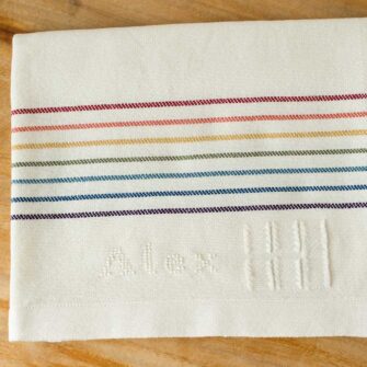 Swans Island Company's Double Rainbow Baby Blanket. Handwoven in Maine with soft 100% organic merino wool. Comes in a signature linen box, perfect for gifting. Custom monogramming is available. Shown here with the name Alex embroidered in natural.