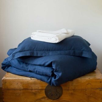 Swans Island Company's Coastal Cottage Bedding Bundle. Includes 1 Classic Linen Sheet Set in white + 1 Relaxed Linen Duvet Set in Midnight Blue. Shown here with our handwoven Firefly blanket in Twilight color.