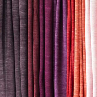 Swans Island Company's Kennebunk Wrap. A luxurious knit wrap made with a silky soft Tussah silk / Merino wool blend. Hand-dyed colors have subtle variegation. 100% Made in USA. Only available at Swans Island Co. Shown here an array of beautiful hand-dyed red, orange and purple colors