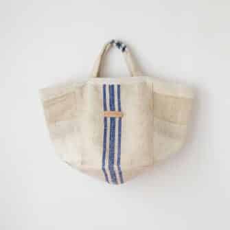 Swans Island Company's Quilt Basket Bag by Govou. Handcrafted in Spain from vintage linen grain sacks. Long canvas shoulder straps and short handles, lined with cotton. Each bag is unique. Shown here in natural with blue stripes