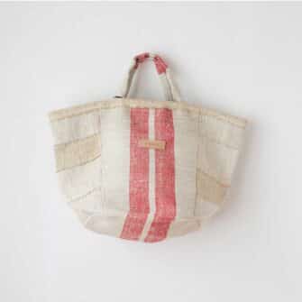 Swans Island Company's Quilt Basket Bag by Govou. Handcrafted in Spain from vintage linen grain sacks. Long canvas shoulder straps and short handles, lined with cotton. Each bag is unique. Shown here in natural with red stripes.