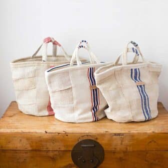 Swans Island Company's Quilt Basket Bag by Govou. Handcrafted in Spain from vintage linen grain sacks. Short handles, lined with cotton. Each bag is unique. Shown here in various natural with red and blue stripes.
