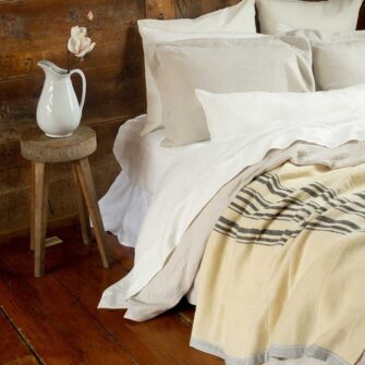 Swans Island Company's Relaxed Linen Bedding. Elegant French linen stitched in the USA for those seeking a refined and timeless sleep experience. Shown here - Relaxed Linen duvet set in Dove paired with our classic linen sheet set in white and a Swans Island handwoven wool Winter Grace Blanket in natural with charcoal stripes.