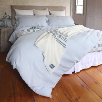seeking a refined and timeless sleep experience. Shown here - bedding bundle including sheet set and duvet cover with shams in Sea Spray, paired with our wool handwoven Grace Blanket in natural with indigo stripe.