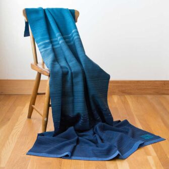 Swans Island Company's Neptune Throw. Handwoven in Maine with a blend of 85% organic merino 15% alpaca. A trio of unique hand-dyed colors in 3 ocean-inspired designs. Show here in Blue with Teals.