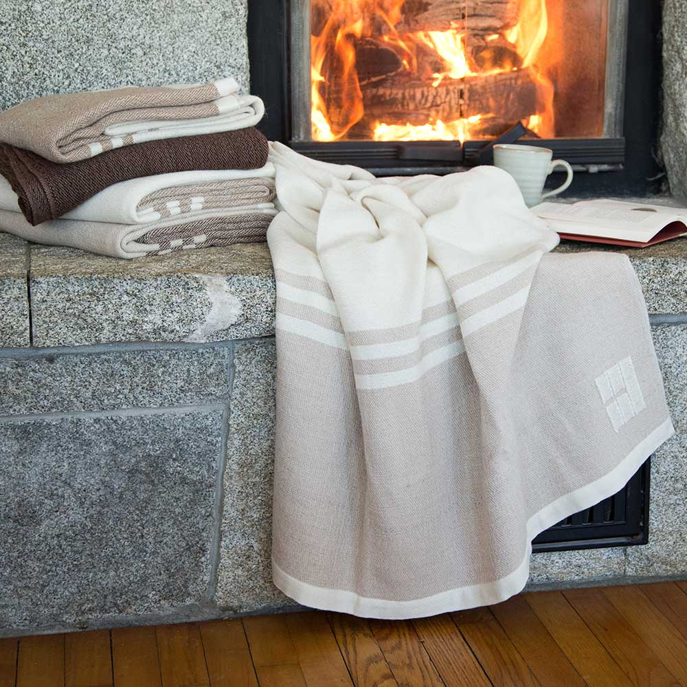 Stormsteg Farm x Swans Island Ltd. Edition Throw. Handwoven in Maine with fiber from Stormsteg, a local alpaca sanctuary. Undyed natural colored fiber. Shown here in a range of beautiful undyed neutral colors, stacked by a roaring fire.