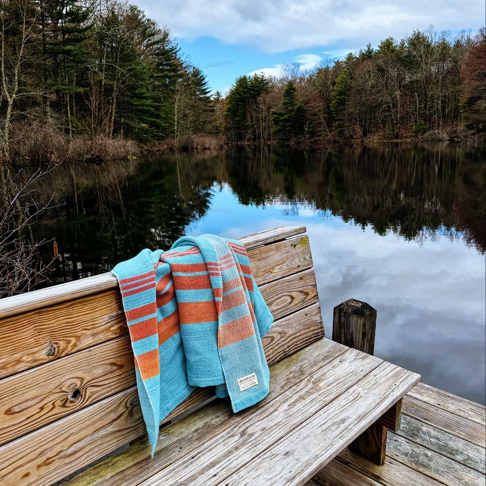 Swans Island x Pierrepont Hicks Wool Camp Blanket - handwoven in Maine with hand-dyed wool. Inspired by camp blankets of the past, woven in colors of today - a bold turquoise ground with shades of orange stripes in the borders. Bring back memories of Maine camp adventures - blue water, orange sunsets.