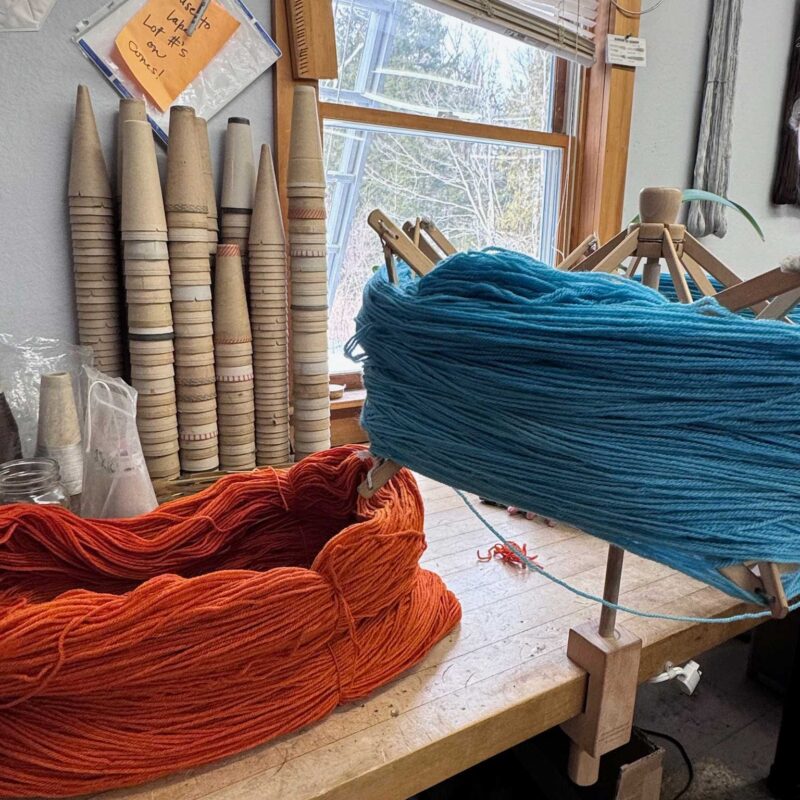 Swans Island x Pierrepont Hicks Wool Camp Blanket - handwoven in Maine with hand-dyed wool. Inspired by camp blankets of the past, woven in colors of today - a bold turquoise ground with shades of orange stripes in the borders. Colorful skeins of hand-dyed wool yarn are prepared for weaving.
