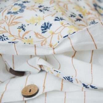 Swans Island Abha Duvet Cover by Soil to Studio. Block printed by hand in India with bright playful patterns. Shown here in natural with gold and blue floral. Closeup of button closure.