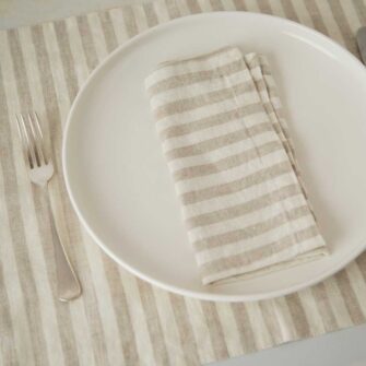 Swans Island Company's linen placemats by Linen Tales, made with 100% European Linen Oeko-Tex® and EUROPEN FLAX® certified. Made with stonewashed soft linen with mitered corners for a crisp edge. Shown here in Natural White Stripe with matching linen napkin.