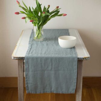 Swans Island Company's linen table runner by Linen Tales, made with 100% European Linen Oeko-Tex® and EUROPEN FLAX® certified. Made with stonewashed soft linen with mitered corners for a crisp edge. Shown here in Blue Fog color on a white enamel table with Red tulips and a white bowl.