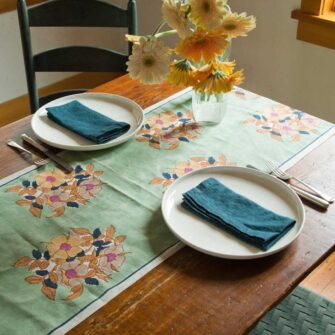 Swans Island Dia Table Runner by Soil to Studio. Block printed by hand in India with bright playful patterns. Shown here in Sage with Yellow floral.