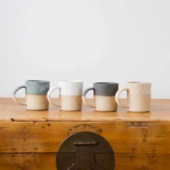 Swans Island Company's Shortie Dipped Mugs are handcrafted with stoneware pottery dipped with a food-safe earthy glaze on top. Made in Maine. Shown here in Sage, White, Charcoal, Natural.