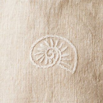 Swans Island Company's Embroidered Quilt Basket Bag by Govou. Upcycled antique grain sacks are reimagined into unique tote bags. This one features a hand-stitched nautilus shell embroidery motif. Shown here in natural colorway. Swatch