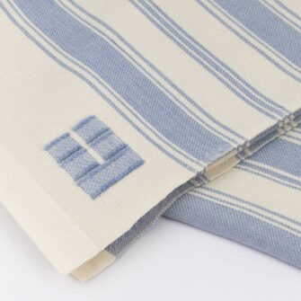 Casa Branca x Swans Island - Branca Stripe Throw . 100% soft merino wool with hand-dyed stripes and ivory silk binding. Handwoven in Maine. Shown here in Sky Blue.