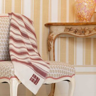Casa Branca x Swans Island - Branca Stripe Throw . 100% soft merino wool with hand-dyed stripes and ivory silk binding. Handwoven in Maine. Shown here in Winterberry, draped on a chair with matching Casa Branca wallpaper in the backgorund.