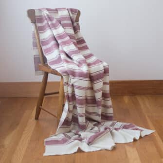 Casa Branca x Swans Island - Branca Stripe Throw . 100% soft merino wool with hand-dyed stripes and ivory silk binding. Handwoven in Maine. Shown here in Winterberry draped on a chair.