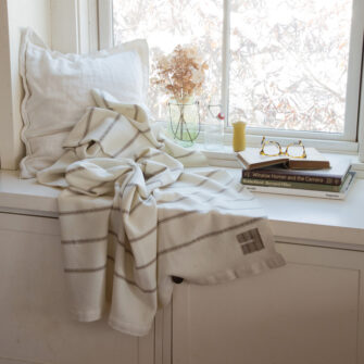 Casa Branca x Swans Island - Branca Ticking Stripe Throw . 100% soft merino wool with hand-dyed stripes and ivory silk binding. Handwoven in Maine. Shown here in Biscotti.